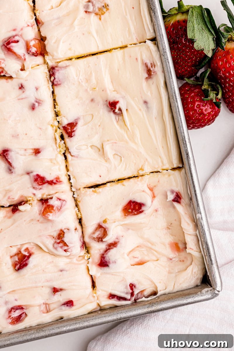 An inviting overhead shot of a freshly baked strawberry sheet cake, beautifully sliced into neat portions within its rectangular baking pan, ready to be served.