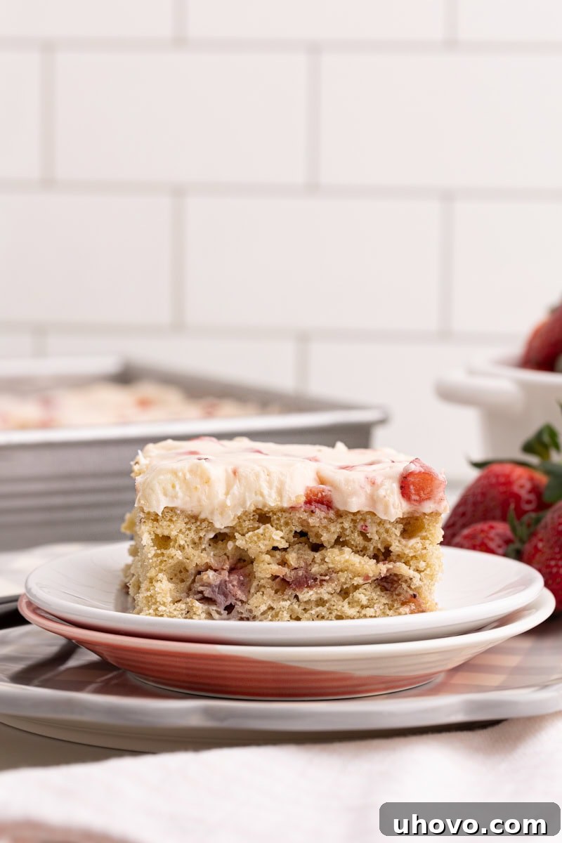 A charming slice of strawberry sheet cake neatly presented on a small stack of elegant white plates, ready for a delightful indulgence.