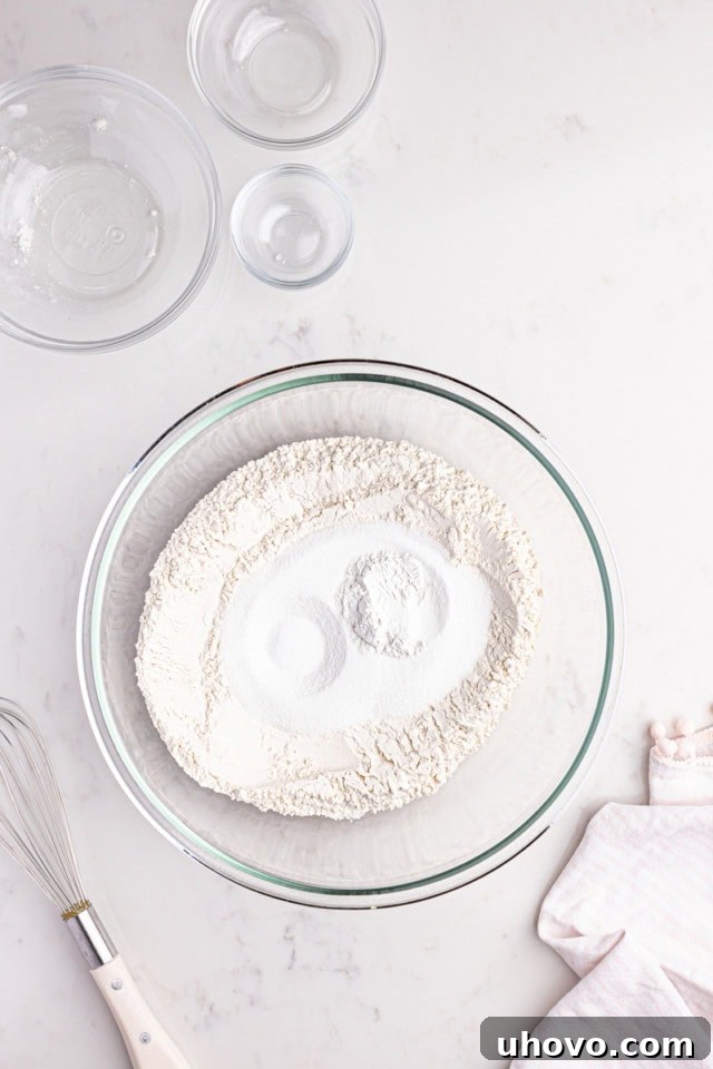 An overhead view showcasing flour, baking powder, and salt precisely measured and combined in a clear glass mixing bowl, representing the initial dry ingredients for the strawberry sheet cake.
