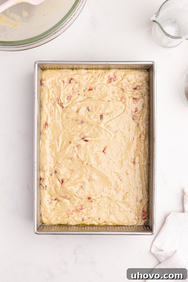 An overhead perspective of smooth strawberry cake batter evenly spread within a rectangular baking pan, glistening and ready to be placed into the oven for baking.