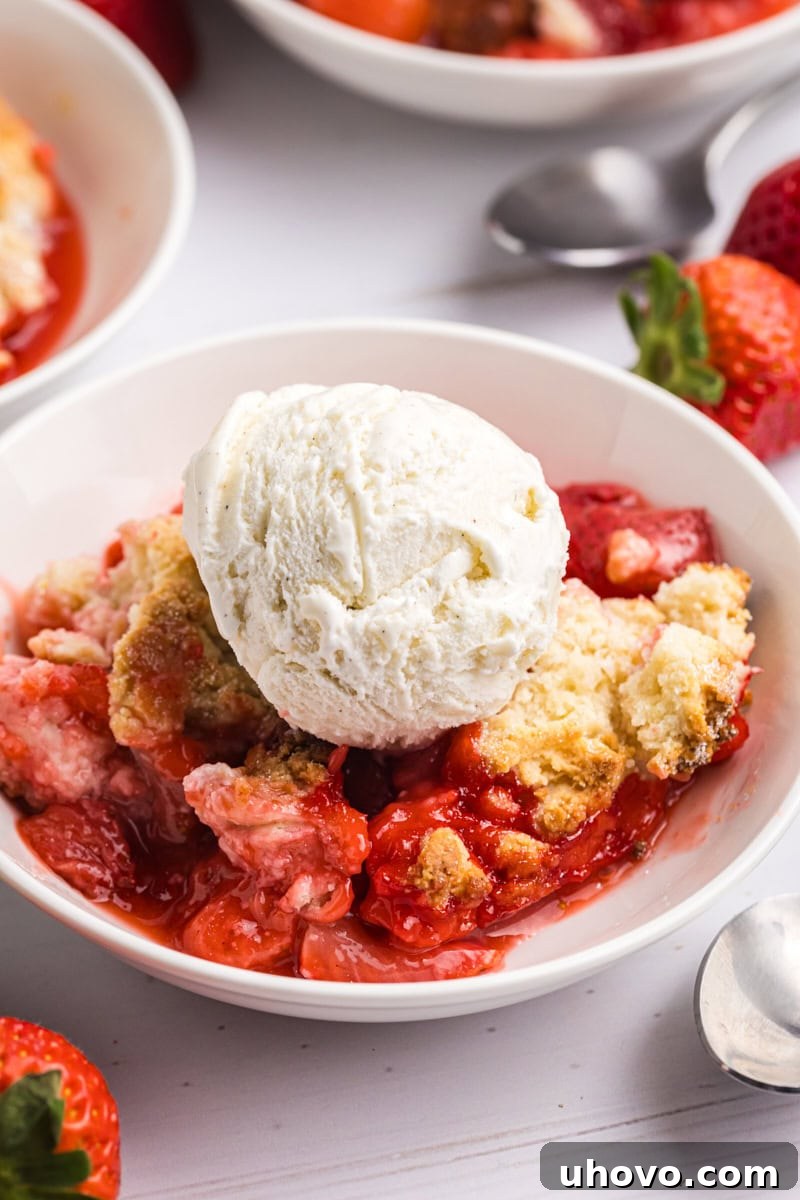 A comforting bowl of homemade Strawberry Cobbler, generously topped with a scoop of melting vanilla ice cream, creating a perfect balance of warm and cold textures.