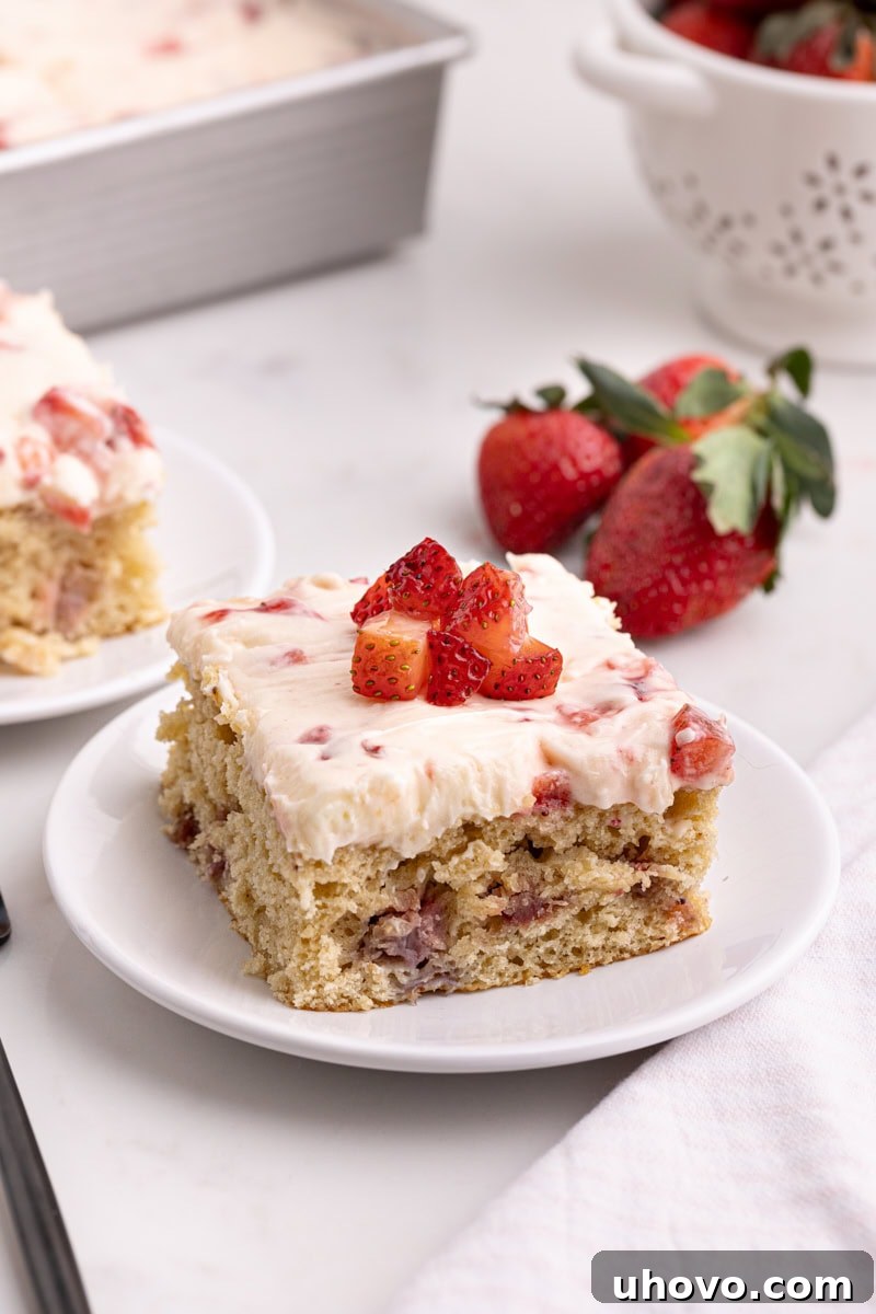 A perfectly portioned slice of Strawberry Sheet Cake on a pristine white plate, showcasing its vibrant pink hue and a generous layer of strawberry frosting.