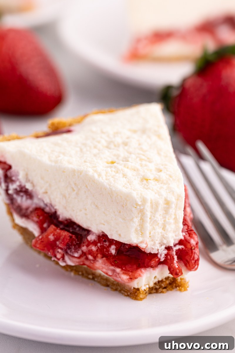 A slice of fluffy Strawberry Icebox Pie on a plate, with a corner taken out, revealing its creamy layers and graham cracker crust.