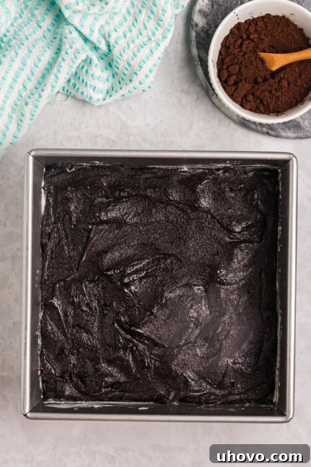 overhead view of dark cocoa brownie batter spread in a square baking pan ready to go into the oven