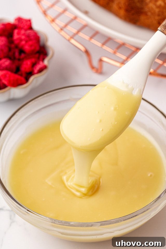 A glass bowl containing freshly made white chocolate ganache, with a spatula lifting a swirl of the glossy mixture, demonstrating its smooth consistency.