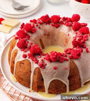 White Chocolate Raspberry Bundt Cake on a white cake plate, garnished with fresh raspberries.