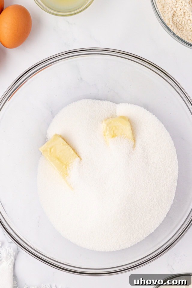 A close-up, overhead shot of softened butter and granulated sugar being creamed together in a glass mixing bowl, illustrating the initial wet ingredient step.