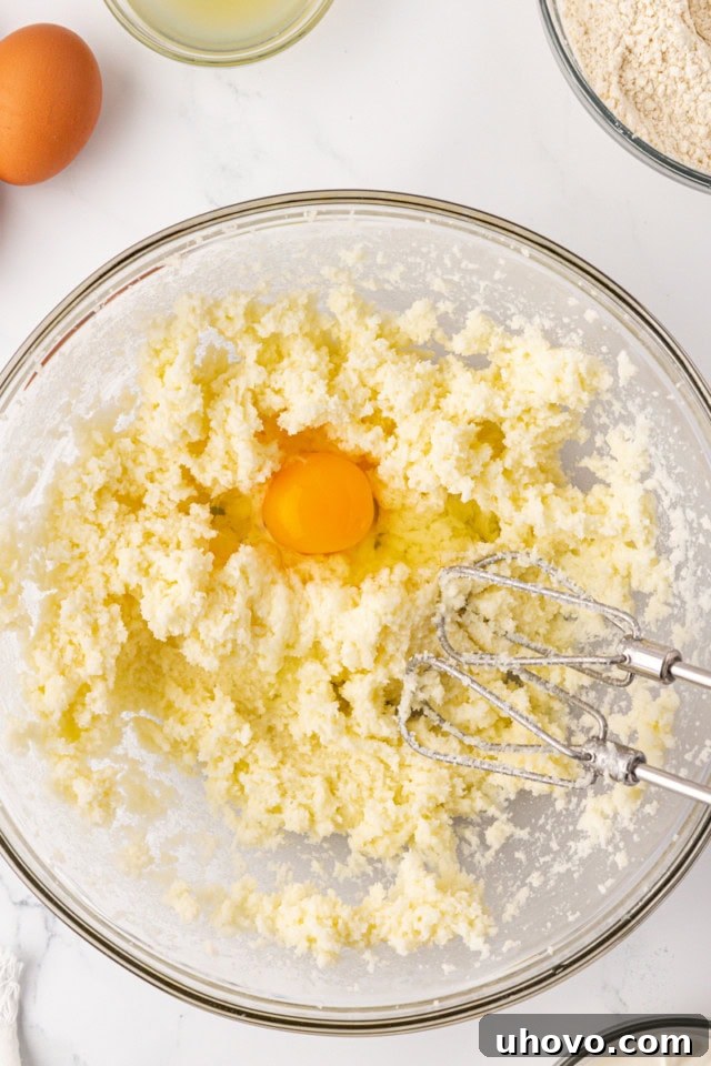 An egg being carefully added to the creamed butter and sugar mixture in a glass mixing bowl, highlighting the egg incorporation process.