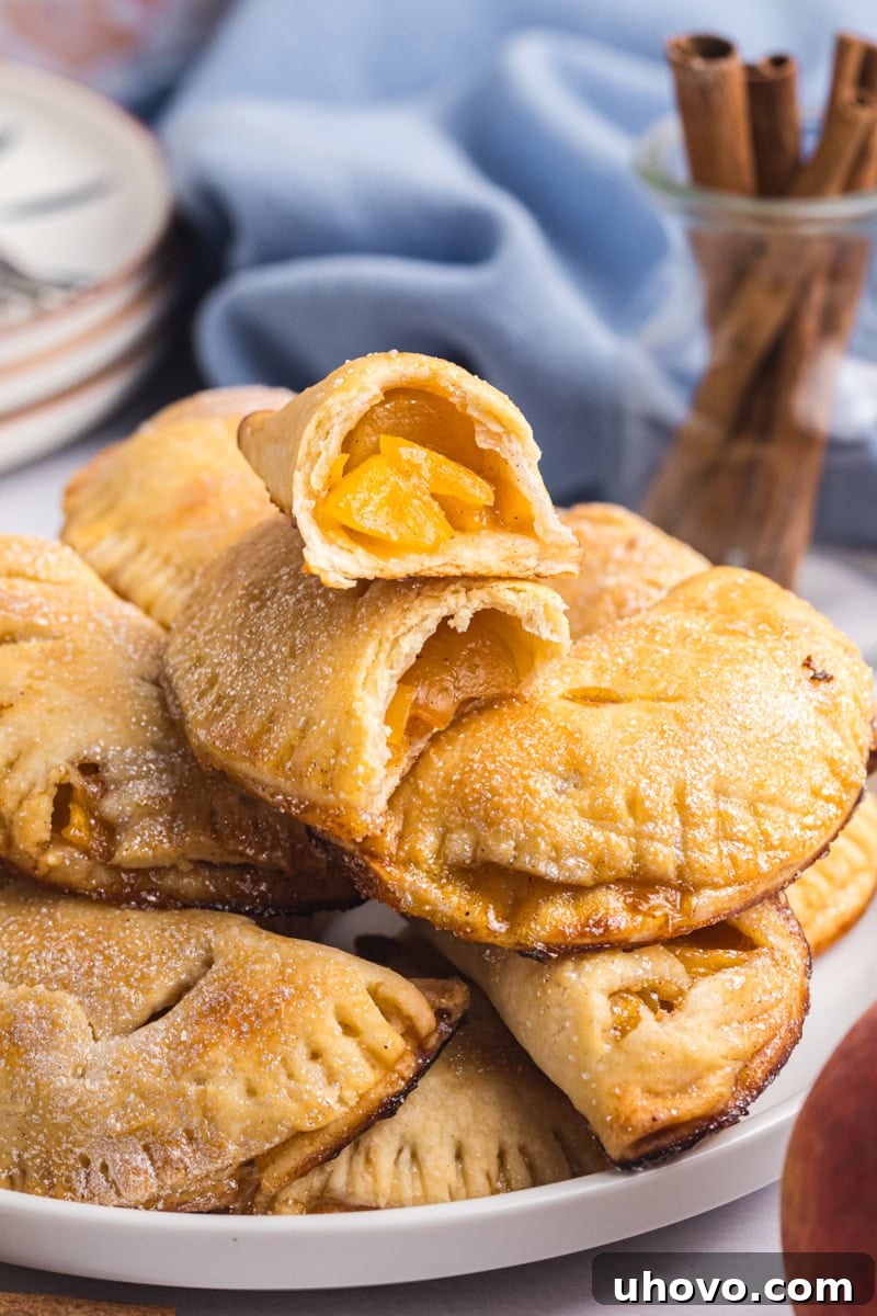 peach hand pies piled on a plate with the top pie cut in half to show the filling