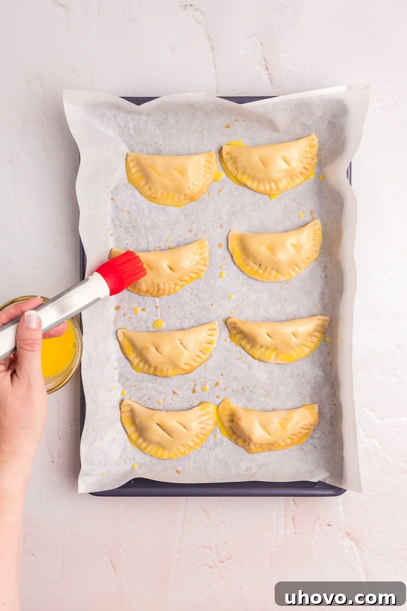 peach hand pies being brushed with egg wash on a baking sheet before going into the oven