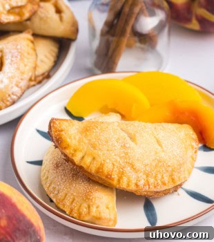 two peach hand pies on a plate with more pies and sliced peaches in the background
