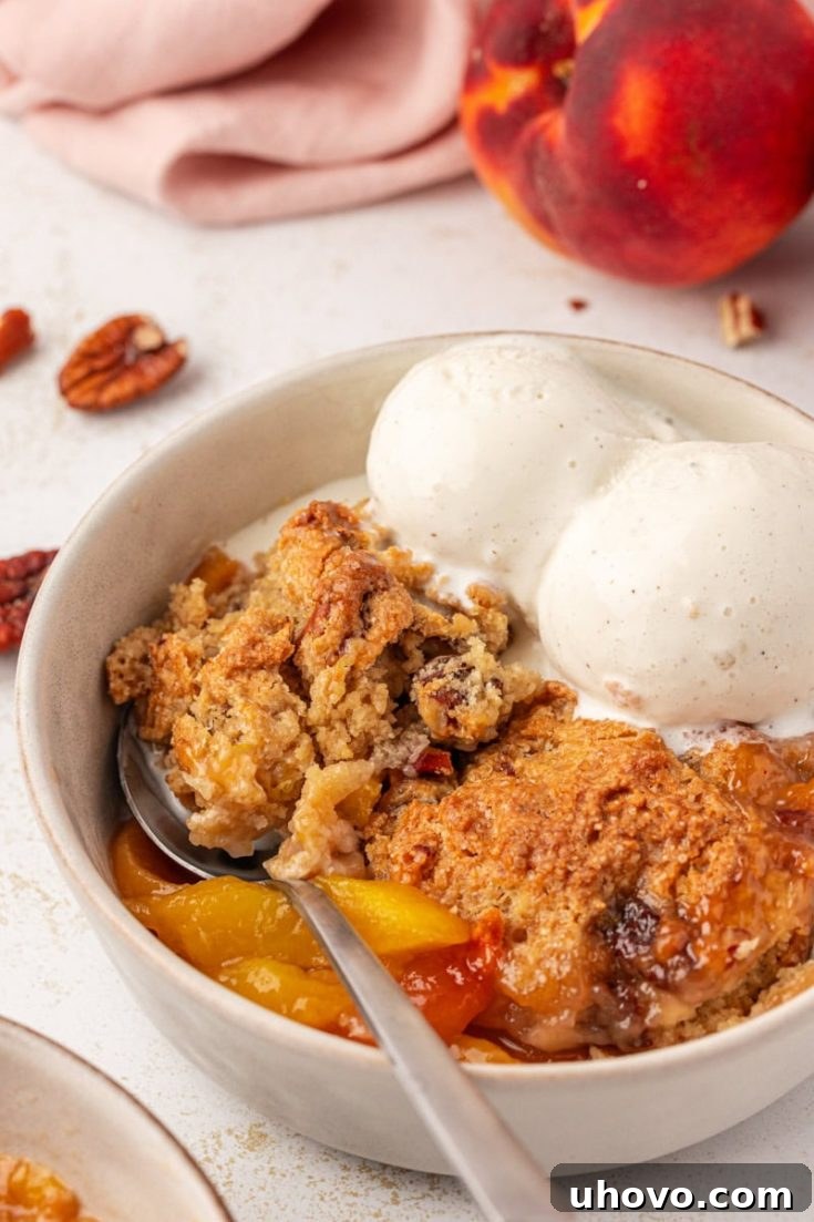 A slice of warm Ginger Peach Cobbler topped with a scoop of vanilla ice cream.