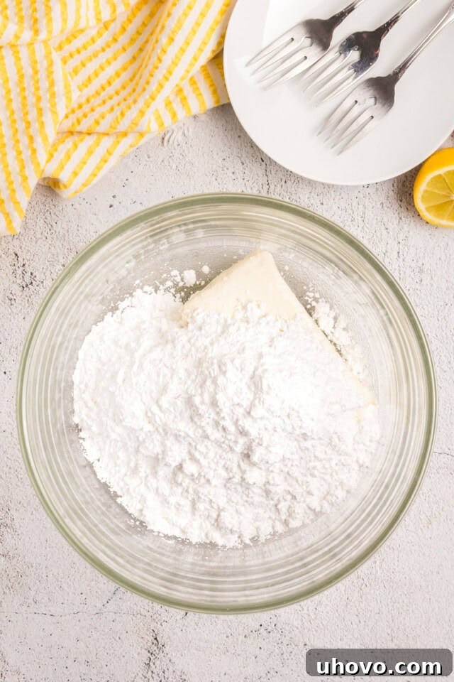 Overhead view of softened cream cheese and sifted confectioners' sugar in a mixing bowl, ready to be beaten for the frosting.