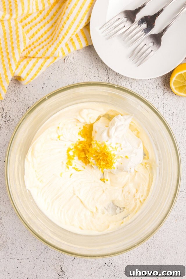 Overhead view of sour cream and lemon zest being added to the cream cheese and sugar mixture for the frosting.