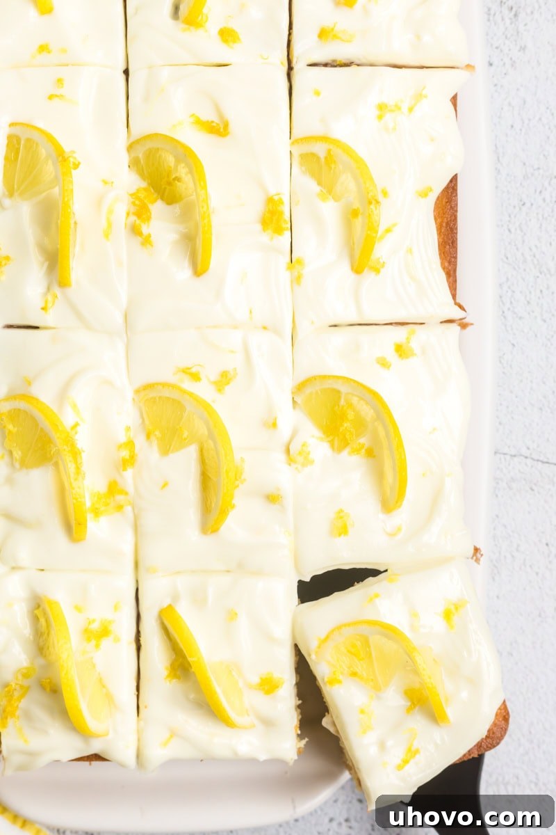 Overhead view of a perfectly sliced lemon sheet cake adorned with creamy lemon cream cheese frosting, delicate lemon slices, and aromatic lemon zest.