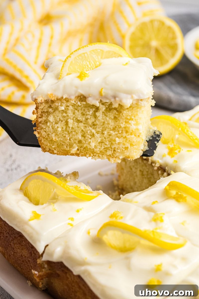 A slice of lemon sheet cake being lifted from the remaining cake on a cake server, showing its enticing texture.