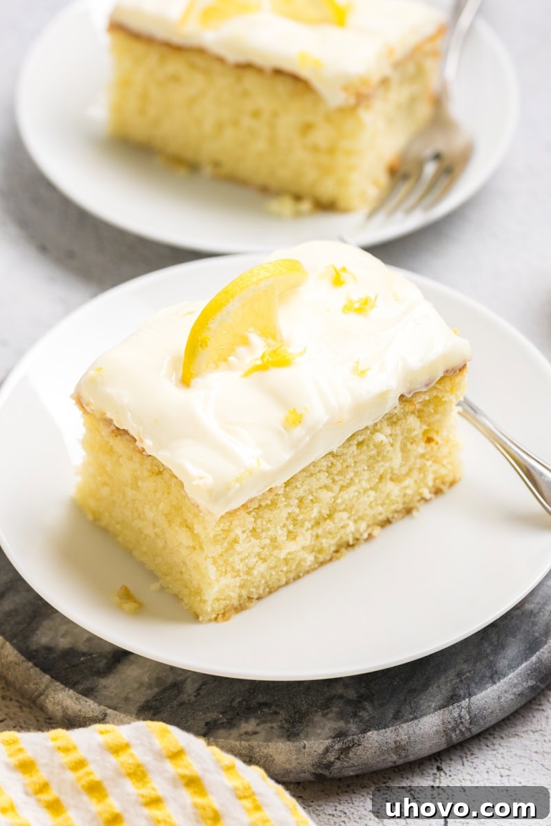 A single slice of lemon sheet cake with lemon cream cheese frosting, elegantly presented on a white plate, inviting indulgence.