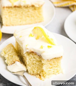 A slice of lemon sheet cake and a bite on a fork on a white plate, highlighting its deliciousness.