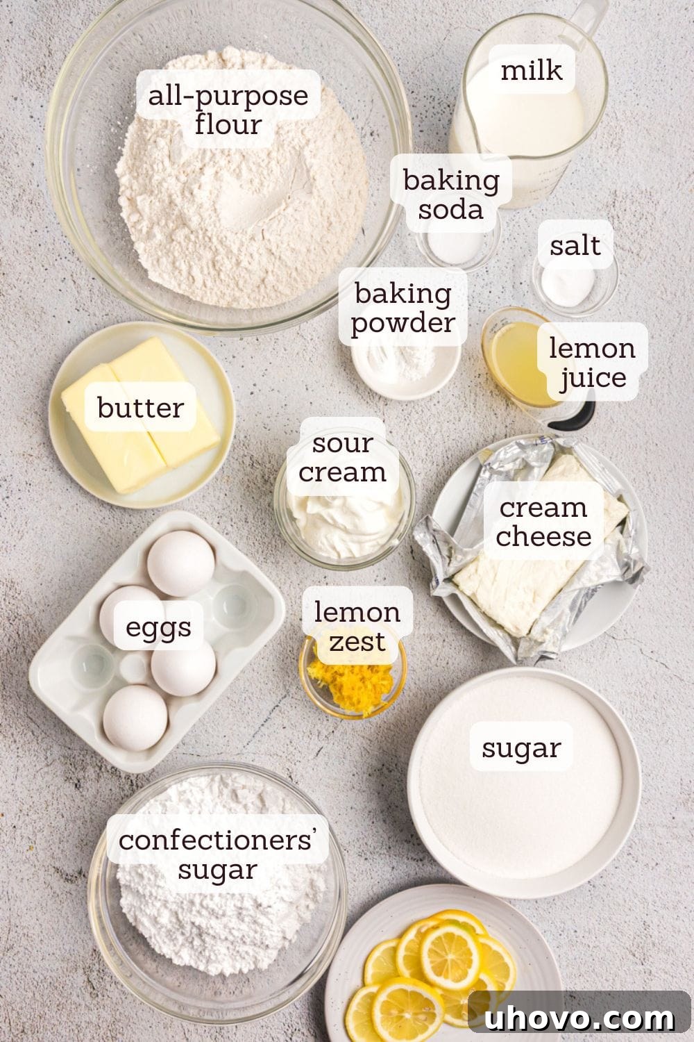 Overhead view of various key ingredients for lemon sheet cake laid out, including fresh lemons, butter, eggs, milk, and flour.