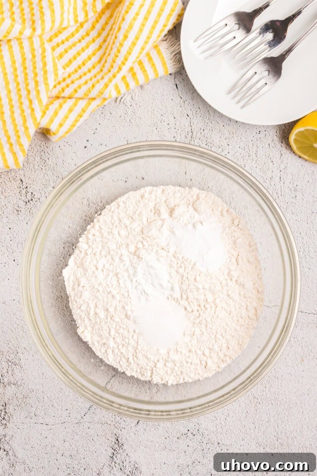 Overhead view of flour, baking powder, baking soda, and salt measured into a mixing bowl, ready to be whisked together.