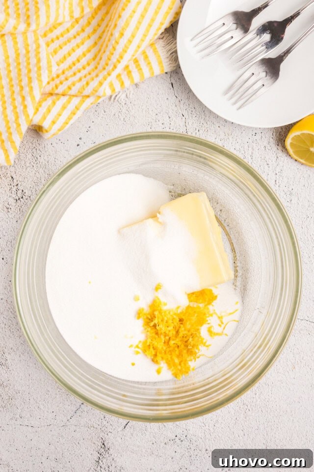 Overhead view of softened butter, granulated sugar, and fresh lemon zest in a mixing bowl, being creamed together.