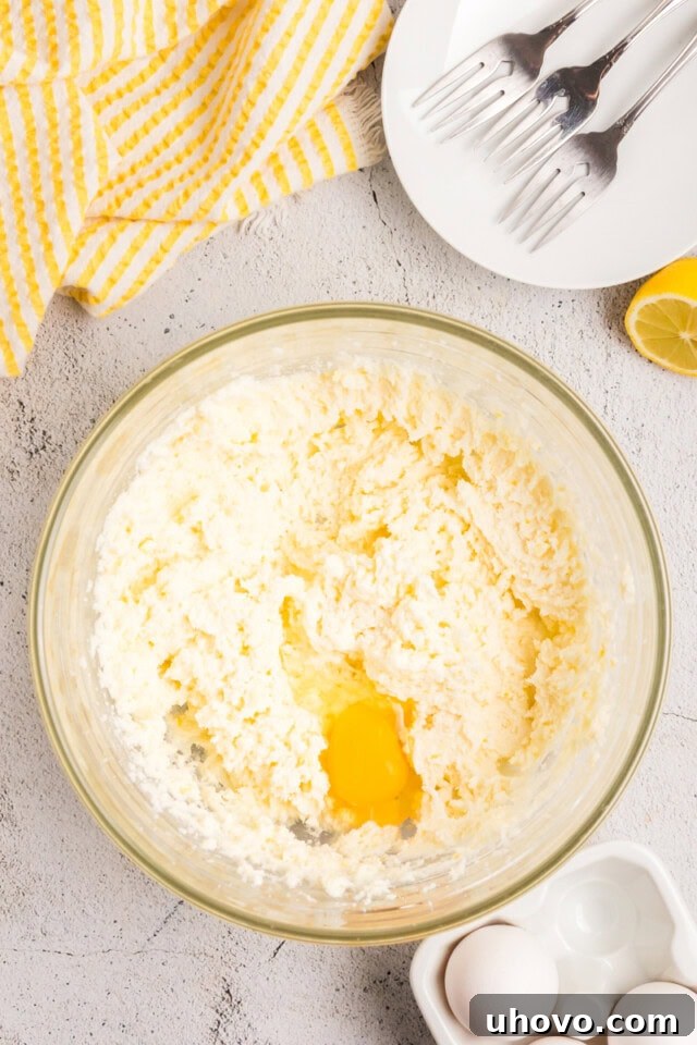 Overhead view of a cracked egg being added to the creamed butter and sugar mixture, ready for mixing.