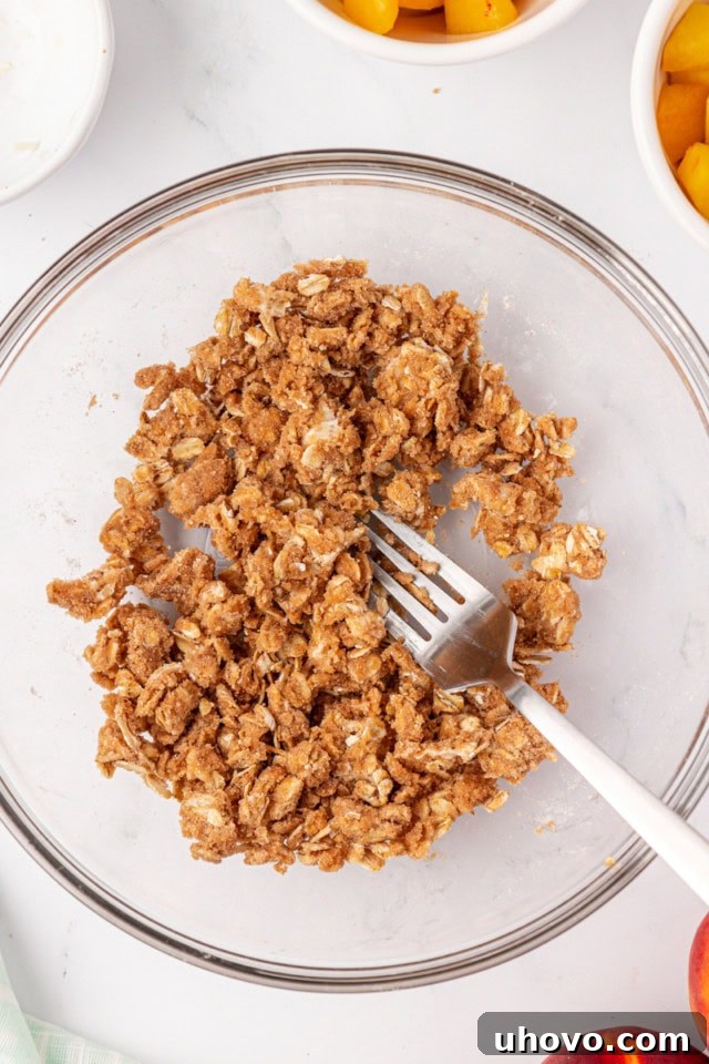 A close-up, overhead view of the crisp topping mixture in a glass bowl after being mixed with butter, showing the desired crumbly texture before being sprinkled over the peaches.