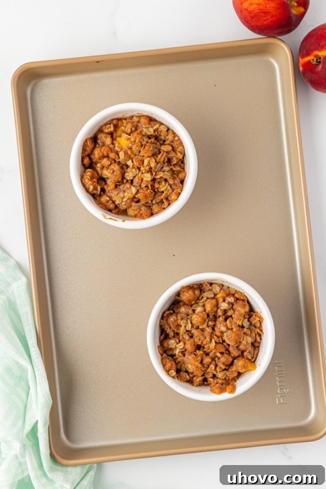An overhead view of two freshly baked small-batch peach crisps, golden brown and bubbling, still on the baking sheet, indicating they are perfectly cooked and ready to be served.