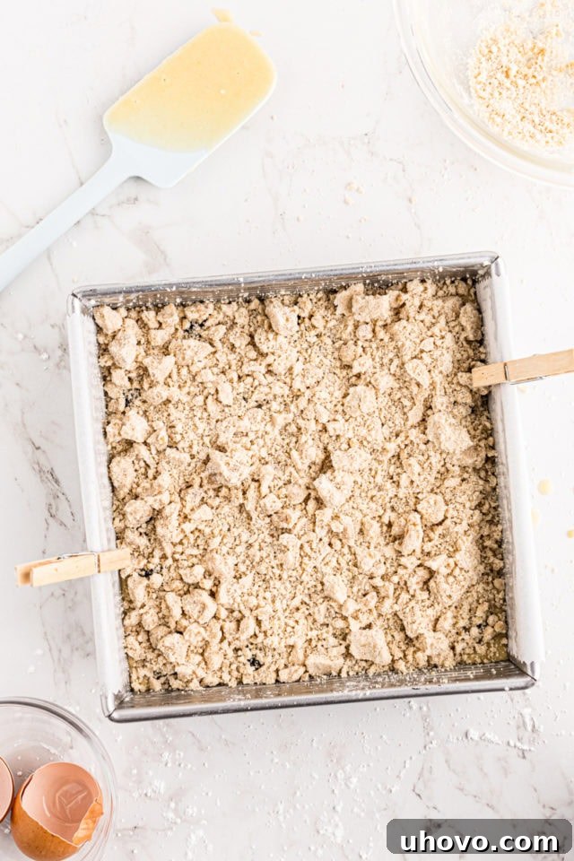 Overhead view of the crumb topping being added over the blackberries and batter in a square baking pan, just before baking the blackberry crumb bars.