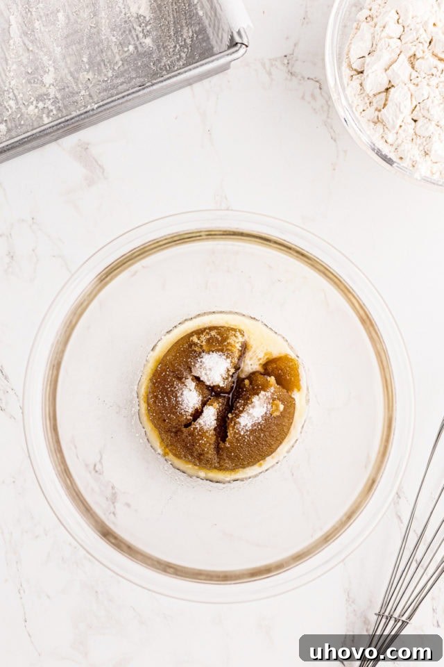 Overhead view of brown sugar, melted butter, and salt being combined in a clear glass mixing bowl, forming the initial steps for the crumb topping of blackberry crumb bars.