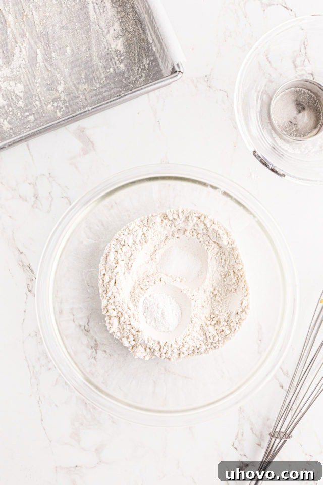 Overhead view of flour, baking powder, and salt measured into a glass mixing bowl, representing the dry ingredients for the blackberry crumb bar batter.