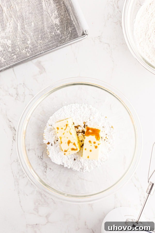 Overhead view of softened butter, confectioners' sugar, and vanilla extract being mixed in a glass bowl, forming the wet ingredients for the blackberry crumb bar batter.