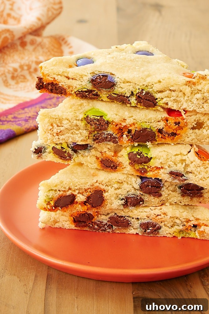 Several M&M sugar cookie bars neatly arranged on a cheerful orange plate, highlighting their soft texture and colorful candy pieces.