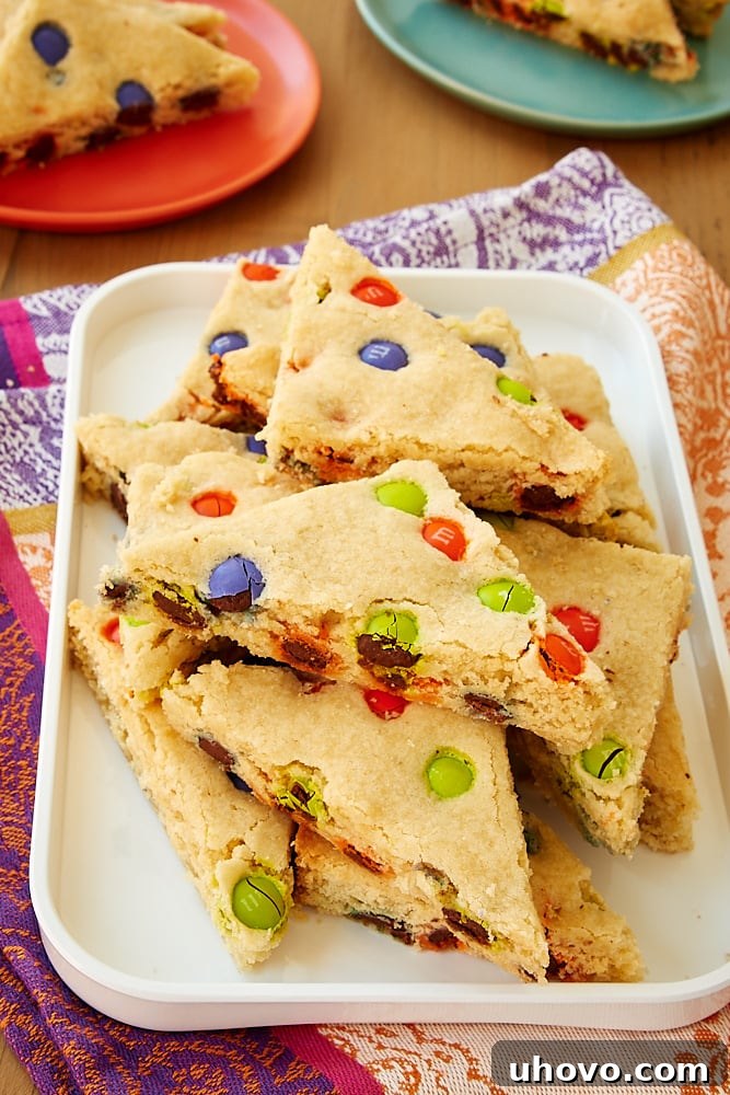 A stack of golden-brown M&M sugar cookie bars, topped with colorful candies, resting on a clean white tray, ready to be enjoyed.