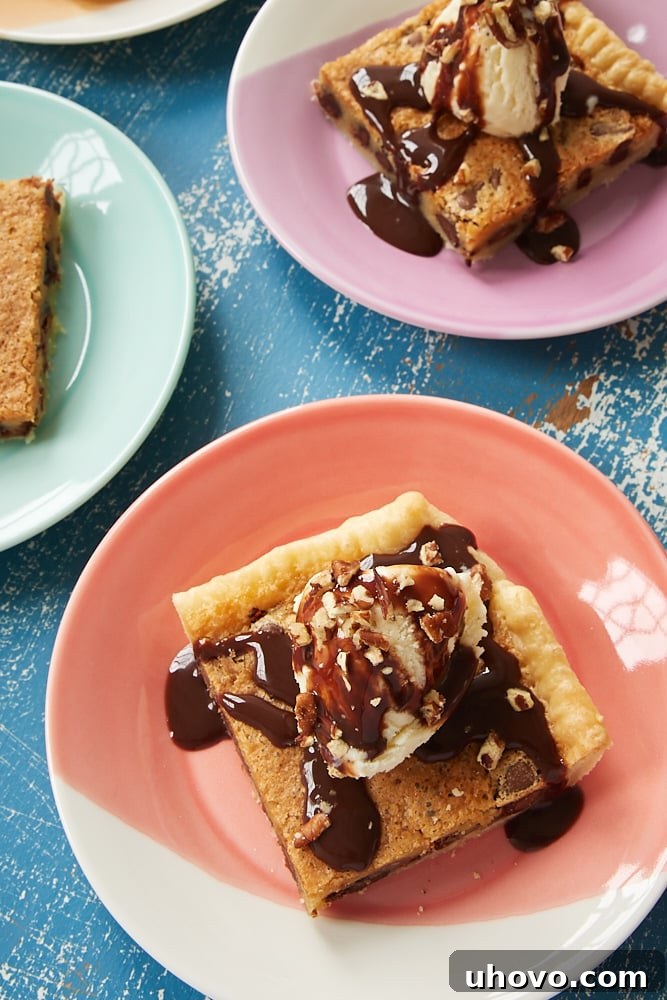 A delectable slice of Double Chocolate Chip Slab Pie, served warm and generously adorned with a scoop of melting vanilla ice cream, drizzled with rich chocolate syrup, and sprinkled with crunchy nuts on a white plate.