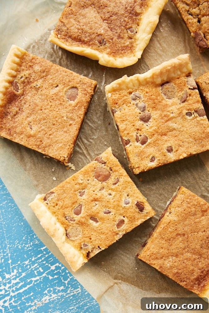 Numerous square slices of Double Chocolate Chip Slab Pie, showcasing their golden crust and abundant chocolate chips, neatly arranged on a piece of parchment paper, highlighting their perfect portioning.