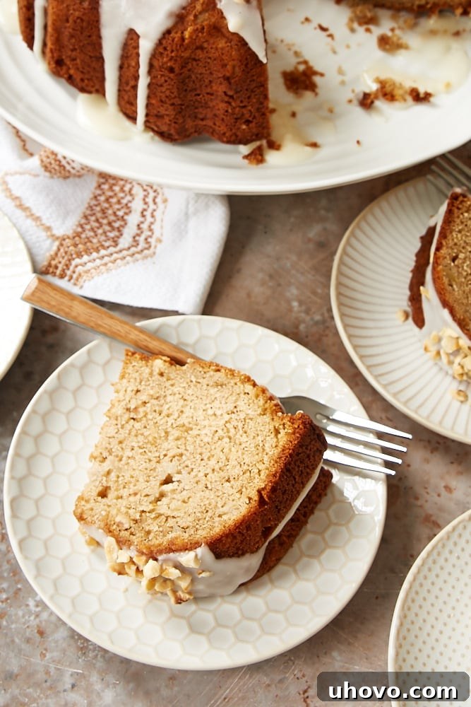 A beautifully presented slice of Hazelnut Pear Bundt Cake, showcasing the tender pear pieces and toasted hazelnuts within the moist crumb. It's topped with a generous drizzle of the luscious sour cream glaze.