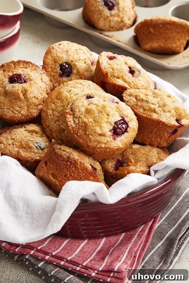 Cranberry Orange Muffins piled high in a napkin-lined red bowl, ready to be enjoyed.