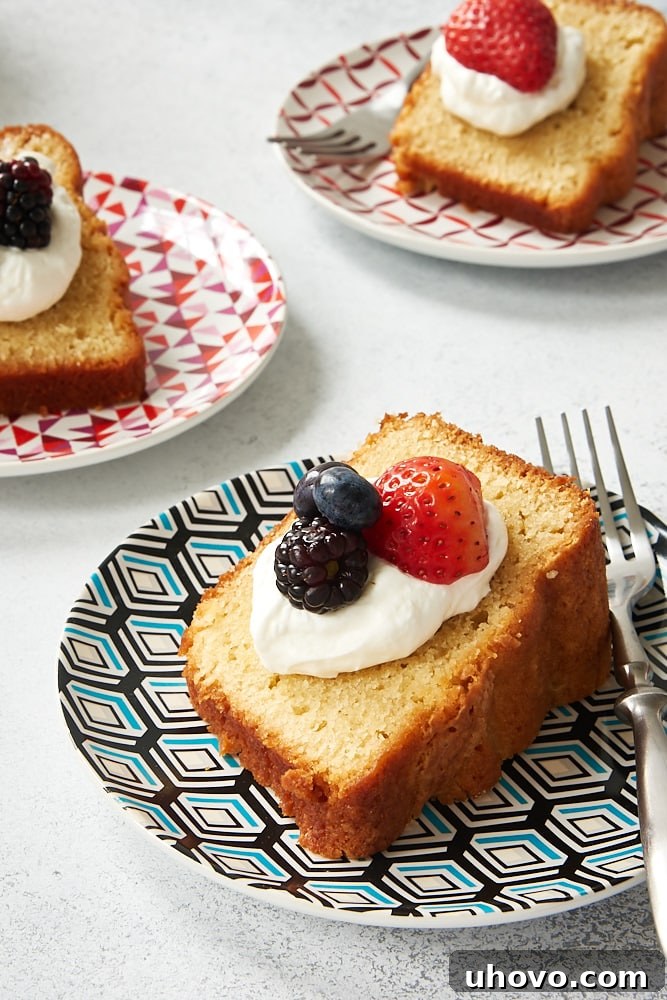 A delectable slice of Sour Cream Pound Cake, beautifully topped with sweetened whipped cream and an assortment of fresh, vibrant berries, inviting you to indulge.