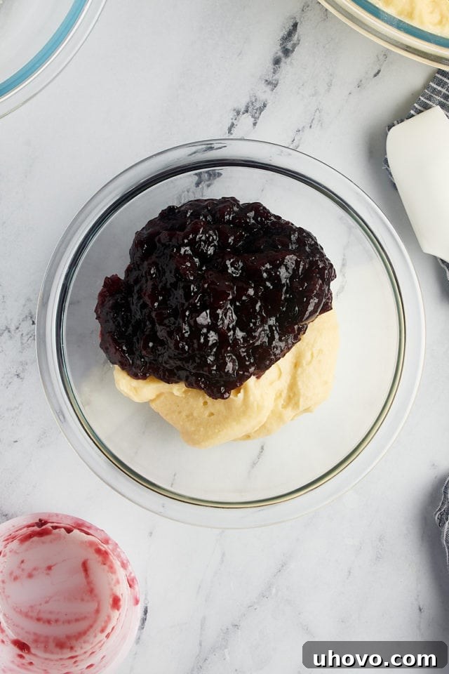 A small portion of cake batter combined with black cherry jam in a glass bowl, creating the vibrant cherry filling.