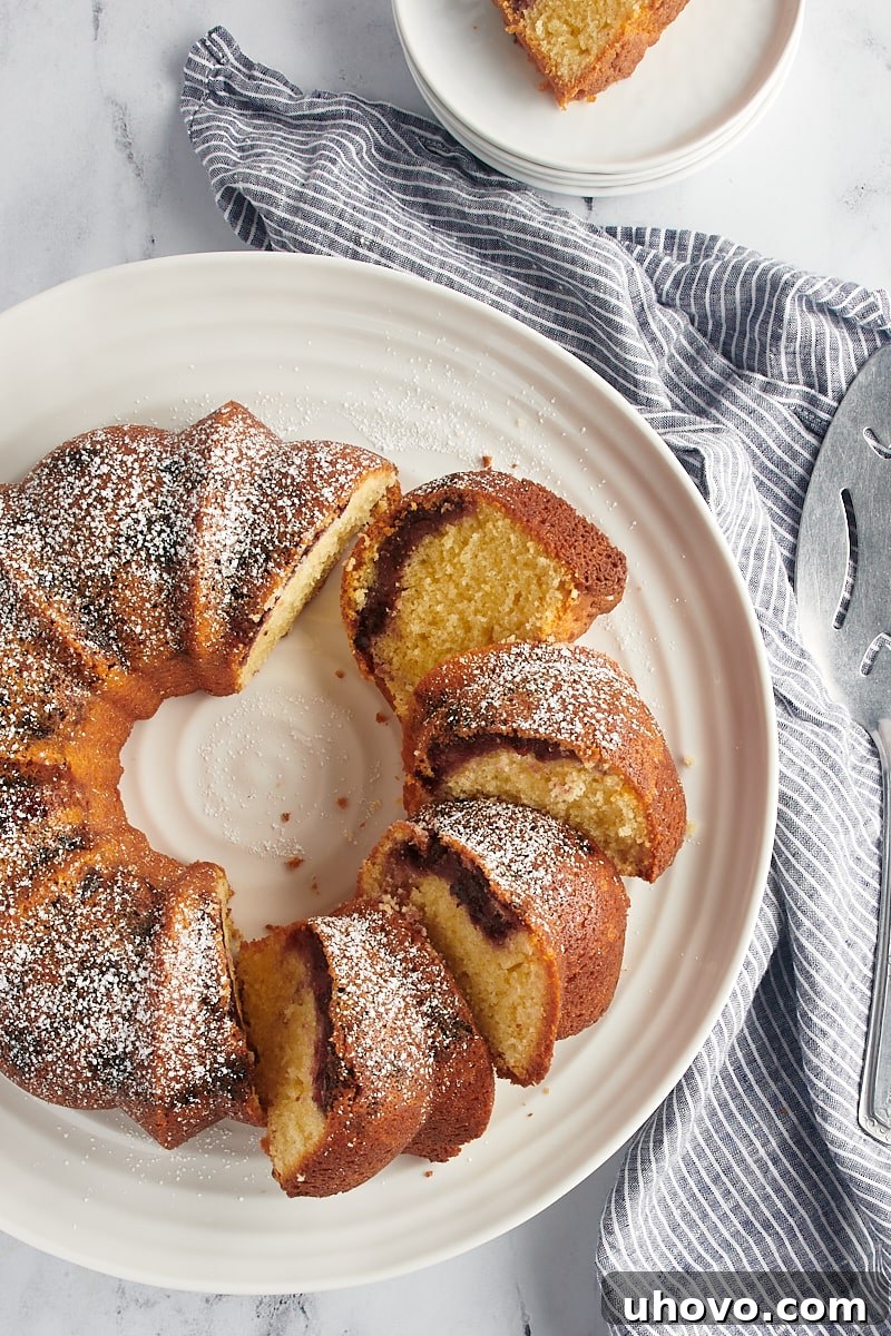An overhead shot of the whole Black Cherry Sour Cream Coffee Cake, partially sliced, resting on a pristine white cake stand.