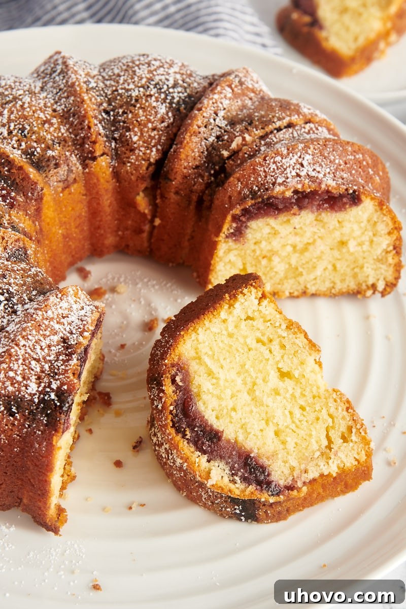 A magnificent Black Cherry Sour Cream Coffee Cake, partially sliced, presented beautifully on a cake stand, ready to be enjoyed.
