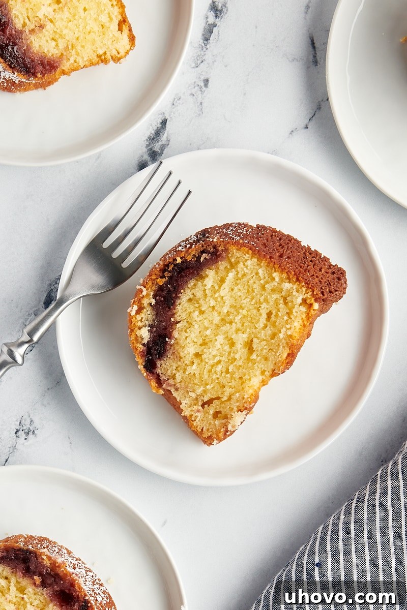 A pristine overhead view of a single slice of Black Cherry Sour Cream Coffee Cake beautifully presented on a white plate, highlighting its moist texture and cherry swirl.