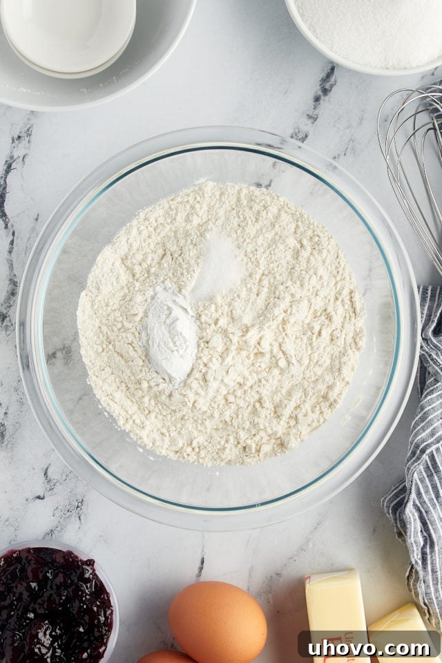 An overhead view of all-purpose flour, baking powder, and salt measured into a clear glass mixing bowl, ready for whisking.