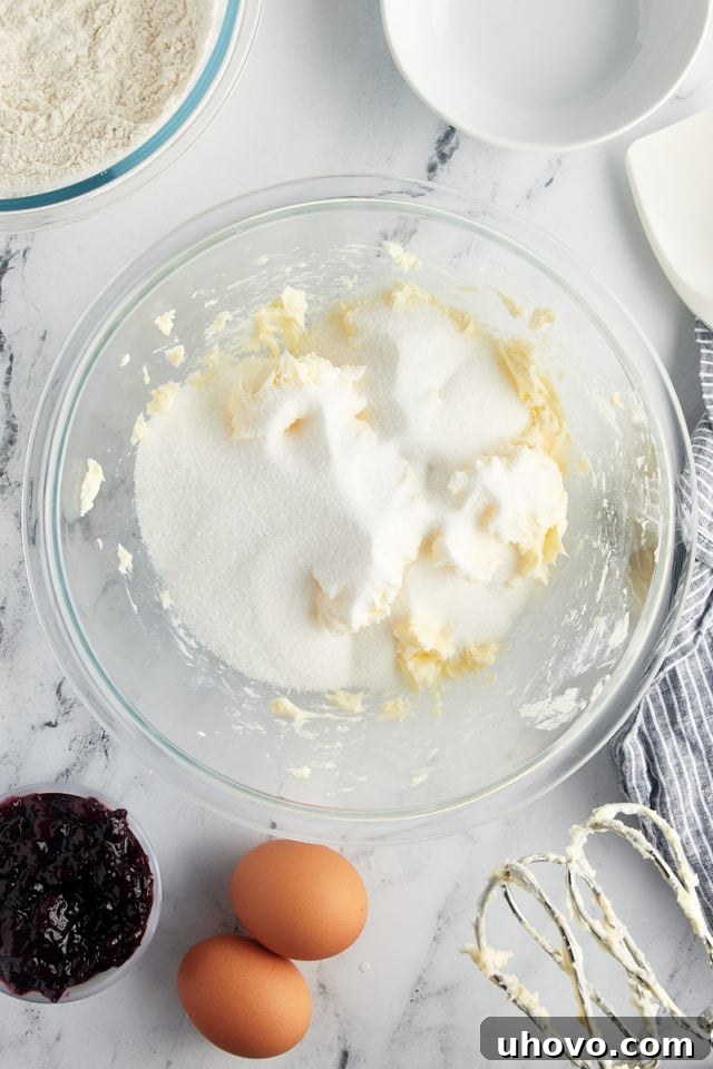 Overhead view of granulated sugar being added to the creamed butter in a glass mixing bowl, ready for beating.