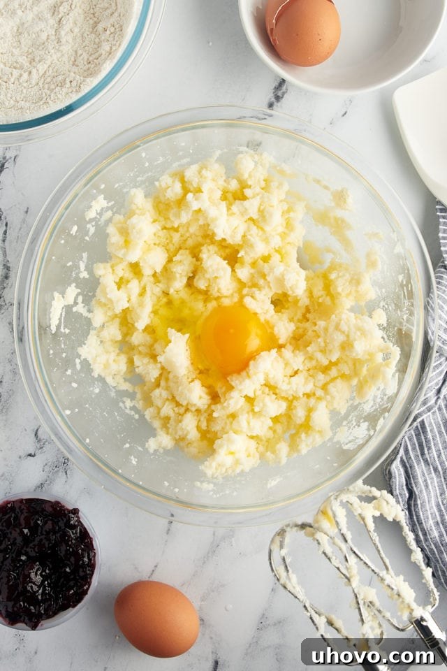 A single egg is being added to the cake batter in a glass mixing bowl, demonstrating the step-by-step process.