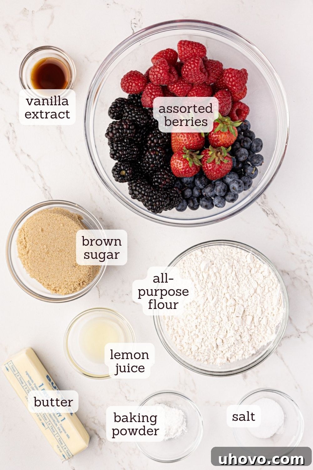 Overhead view of various ingredients meticulously laid out for making mixed berry cobbler, each labeled for easy identification.