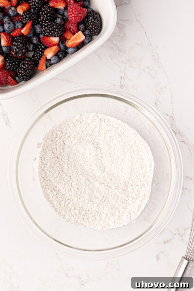 An overhead shot of a mixing bowl containing the dry ingredients for the cobbler topping: flour, baking powder, and salt, ready to be whisked.