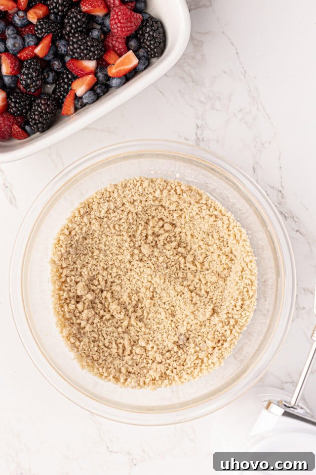 The cobbler topping mixture, now resembling coarse crumbs, rests in a glass bowl after the dry ingredients have been incorporated.