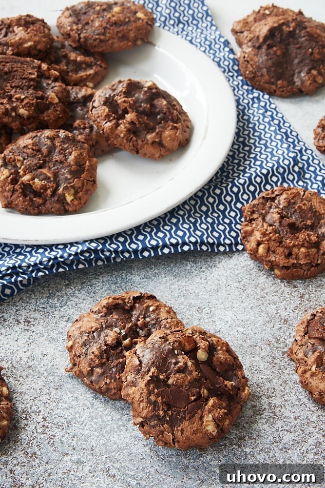Several Flourless Chocolate Hazelnut Cookies scattered on a gray surface, showcasing their cracked tops